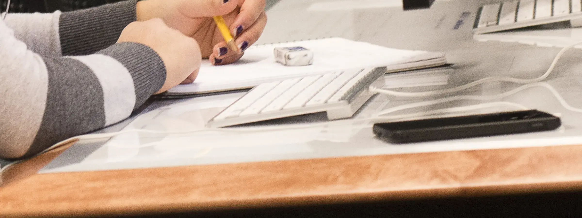 person holding a writing implement using a notepad, sitting in front of a computer 